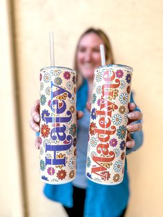 a woman is holding two cups with the word happy on them, both decorated with flowers