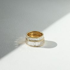 two gold wedding bands with baguettes on them sitting on a white surface in the sun