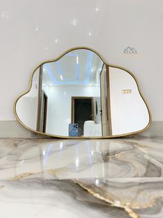 a large mirror sitting on top of a marble counter next to a white wall with gold trim