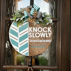 a wooden sign that says knock slowly on the side of a door with a wreath