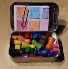 an open tin filled with lots of different colored toy blocks and toys on top of a wooden table