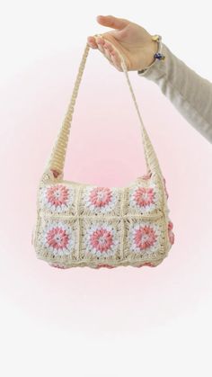 a hand holding a crocheted purse with pink and white flowers on the front