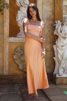 The event dress of the summer has arrived. Meet the Blissful Satin Maxi Dress in Orange. This dress radiates classy nights and sunkissed memories. Style with white heels and gold adornments to complete the look.  Maxi dress, true to size Fabric tie shoulder straps Ruched detail bust  Flowy skirt  Invisible side zipper Semi-lined  100% Polyester  Non-stretch  Please refer to the care label on your garment for specific instructions on how to care for it Model wears XS Length from shoulder to hem: 130cm on an S Chest 37cm, Waist 32cm, size S Neon Orange Bridesmaid Dresses, Ruched Bust Dress, Terra Cotta Wedding Bridesmaid Dresses, Light Orange Dress Long, Summer Bridesmaid Ruched Maxi Dress, Summer Lace Midi Dress For Prom, Summer Prom Midi Dress With Fitted Bodice, Fitted Summer Gala Dress, Glamorous Ruched Dresses For Summer