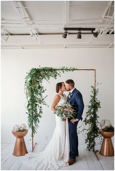 a bride and groom kissing in front of an arch of greenery at their wedding