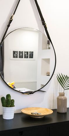 a mirror hanging on the wall next to a table with a plate and potted plant