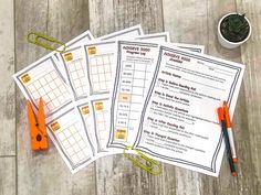 four worksheets with scissors and paper clips on a wooden table next to a potted plant