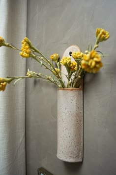 a vase with yellow flowers in it hanging on a wall next to a mirror and curtain