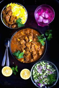 the meal is prepared and ready to be eaten on the table, including rice, onions, lemons, cabbage, and chicken curry