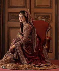 a woman in a red and gold wedding dress sitting on a red chair with her arms crossed