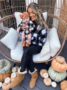 a woman sitting on a chair holding a baby in her lap and surrounded by pumpkins