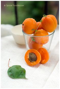 a glass bowl filled with oranges on top of a white table cloth next to a green leaf