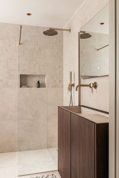 a walk in shower sitting next to a wooden cabinet under a large mirror on the wall