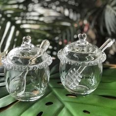 two clear glass jars sitting on top of a green leafy tablecloth with silverware