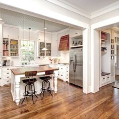 an open kitchen with white cabinets and wood flooring on the wooden floor, along with stainless steel appliances