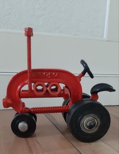 a red toy tractor sitting on top of a wooden floor next to a white wall