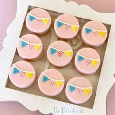 pink cupcakes with yellow and blue bunting on them are in a box