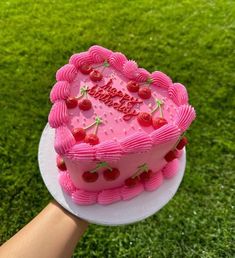 a pink heart shaped cake with strawberries on top is being held by a person's hand