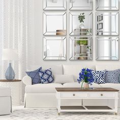 a living room filled with white furniture and mirrors on the wall above it's coffee table