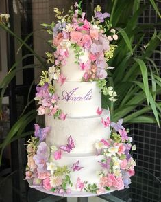 a three tiered wedding cake decorated with pink and purple flowers on a glass table