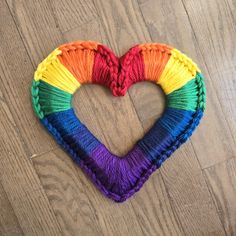 a heart made out of yarn sitting on top of a wooden floor in the shape of a rainbow