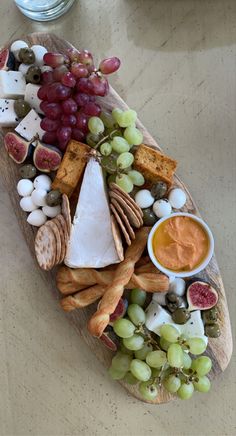 a wooden platter filled with cheese, crackers and grapes