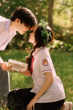 two young people sitting on the ground reading books in front of each other with trees in the background