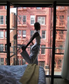 a woman standing on top of a bed in front of a large window next to a building