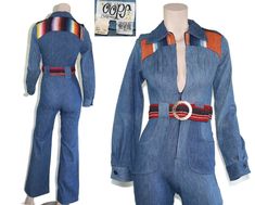 This deadstock 70s-era jumpsuit features a lovely vintage wash denim with western style serape patchwork and shoulder epaulettes on the bodice, matching belt with huge brass "militaires equipment" buckle, interesting 60s/70s style hip pockets, and flared bell bottom pant legs. This piece has never been worn and still has original price tag attached. Jumpsuit is 100% cotton, unlined and zips up the front. Best fits size xxs or xs (please check measurements below). Accessories not included. Payment plans available. Approximate Flat Measurements:  Multiply times 2 for bust, waist, and hip measurements. For best fit, compare with a similar style of clothing which you already own.  Total Length: 56.5" Bodice Length: 15.5" Pant Length: 41" Inseam: 31" Rise: 12" Shoulder to Shoulder: 14" Sleeve L Retro Cotton Fitted Jumpsuits And Rompers, Vintage Jumpsuits And Rompers For Fall, Vintage Fitted Denim Jumpsuit For Summer, Fitted Blue Denim Retro Jumpsuit, Vintage Cotton Fitted Denim Jumpsuit, Retro Fitted Long Sleeve Jumpsuits And Rompers, Spring Vintage Fitted Denim Jumpsuit, Blue Fitted Vintage Denim Jumpsuit, Vintage Fitted Long Sleeve Jumpsuits And Rompers