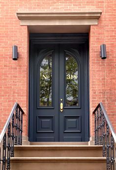 a black front door with two sidelights and wrought iron railing on a brick building