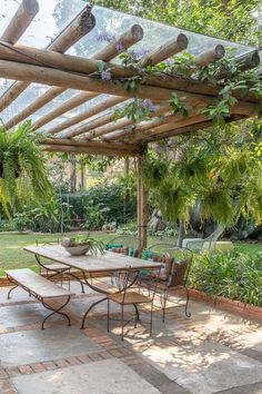 an outdoor dining table and chairs under a pergolated roof in a garden area