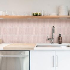 a kitchen with pink tiles and white cupboards, stainless steel dishwasher and sink