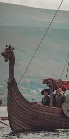 two men are riding in a boat with a dragon on it's side and another man is standing next to the boat