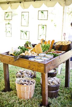 a wooden table topped with lots of food on top of a lush green grass covered field