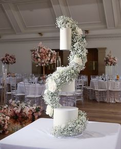 a three tiered wedding cake with white flowers on the top and bottom is surrounded by chairs