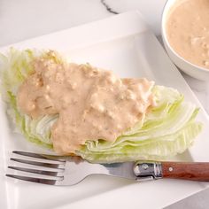 a white plate topped with lettuce and sauce next to a bowl of dressing