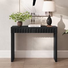 a black console table with two plants on top and a lamp next to it in front of a painting