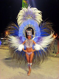 a woman in a blue and white costume with feathers on her head walking down the street