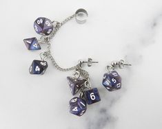 🎲 Carry your love of gaming with you wherever you go when you wear these mini FanRoll stardust galaxy swirl polyhedral dice chained ear cuffs! All seven polyhedral dice are present on the chain and dangling from the posts. These are the perfect fancy and funky accessory for game night, cons, or wherever you feel like showing off your love of gaming and dice. This is a mismatched set with a cuff designed for the right ear (but can be worn on the left as well) with six dice and a post for the other ear with one D20. 🎲 Also available in more colors, please check my other listings for availability. 🎲 Hypoallergenic stainless steel cuff is flexible enough to size to your ear. 🎲 Each order comes ready-to-gift in a white, cotton-filled box and black satin bag. 🎲 We understand accidents happe Dnd Jewelry, Geek Aesthetic, Dice Jewelry, Weird Earrings, Dnd Crafts, Ear Cuff Chain, Adopt Idea, Aesthetic Earrings, Jewelry Ear