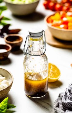 a glass bottle filled with liquid sitting on top of a table next to bowls of vegetables