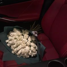 a bouquet of white roses sitting on top of a red seat in the back of a car