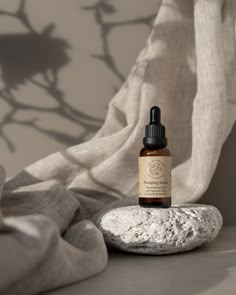 a bottle of essential oil sitting on top of a rock next to a white curtain