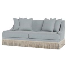 a light blue couch with fringe trimmings and pillows on the back, against a white background