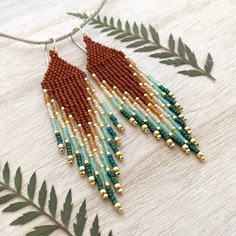 the beaded earrings are hanging from a string on a wooden table with green leaves