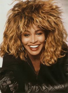 a black and white photo of a woman with curly hair smiling at the camera while wearing a leather jacket