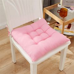 a pink chair cushion sitting on top of a white wooden chair next to a table