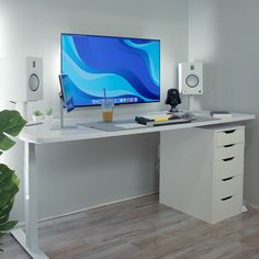 a white desk with a computer monitor and keyboard on it, next to a potted plant