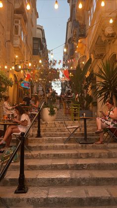 some people are sitting on the stairs in an alleyway with lights hanging above them