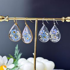 three earrings hanging from a gold rack with flowers on them and daisies in the background