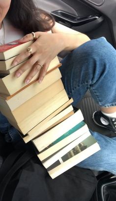 a woman sitting in the back seat of a car while holding a stack of books