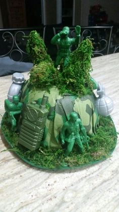 a cake made to look like an army helmet with green moss on the top and soldiers in camouflage